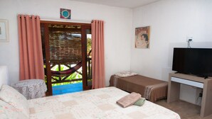 A bedroom with a bed, a desk, a television, and a view of a hammock outside. - Recanto dos Dendês Chalés - Chalé Sol - Praia do Sargi, Serra Grande, Uruçuca. (Uruçuca)