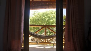 A hammock under a wooden balcony with a view of trees. - Recanto dos Dendês Chalés - Chalé Sol - Praia do Sargi, Serra Grande, Uruçuca. (Uruçuca)