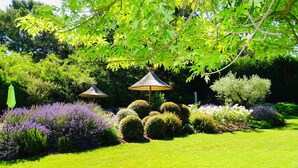 A well-maintained garden with neatly trimmed hedges, a variety of flowering plants, and two thatched umbrellas. - Prestige 5 star villa  (Saint-Rémy-de-Provence)