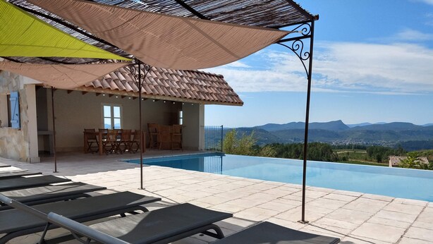 Un espace aménagé au bord de la piscine, avec des chaises longues, une pergola et une vue sur les montagnes.