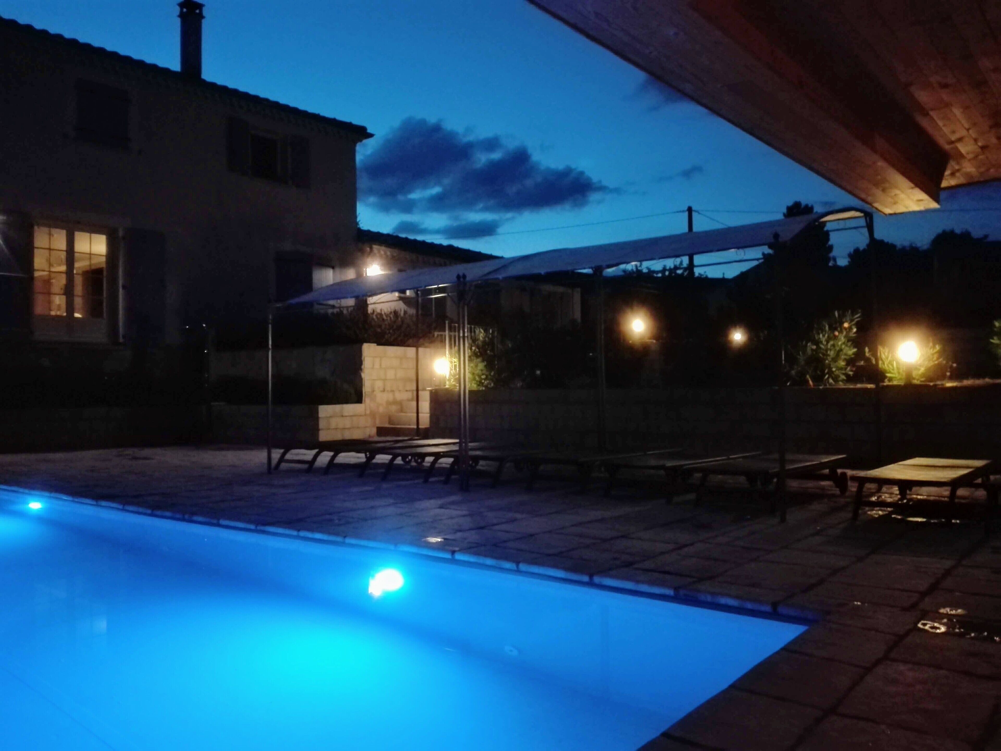 Ein Swimmingpool mit überdachter Terrasse, Sitzgelegenheiten im Freien und einem Haus im Hintergrund.