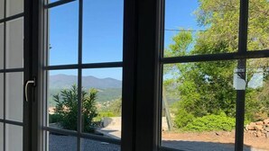 Une vue à travers une fenêtre, avec un ciel dégagé, de la verdure et des montagnes lointaines.
