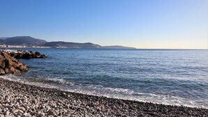 A pebble beach with a view of distant mountains and a clear sky. - 2 Rooms NEW Promenade des Anglais Amazing View (Nice)
