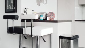 A modern kitchen with a white countertop, two bar stools, a stainless steel trash bin, and a decorative wall piece. - 2 Rooms NEW Promenade des Anglais Amazing View (Nice)