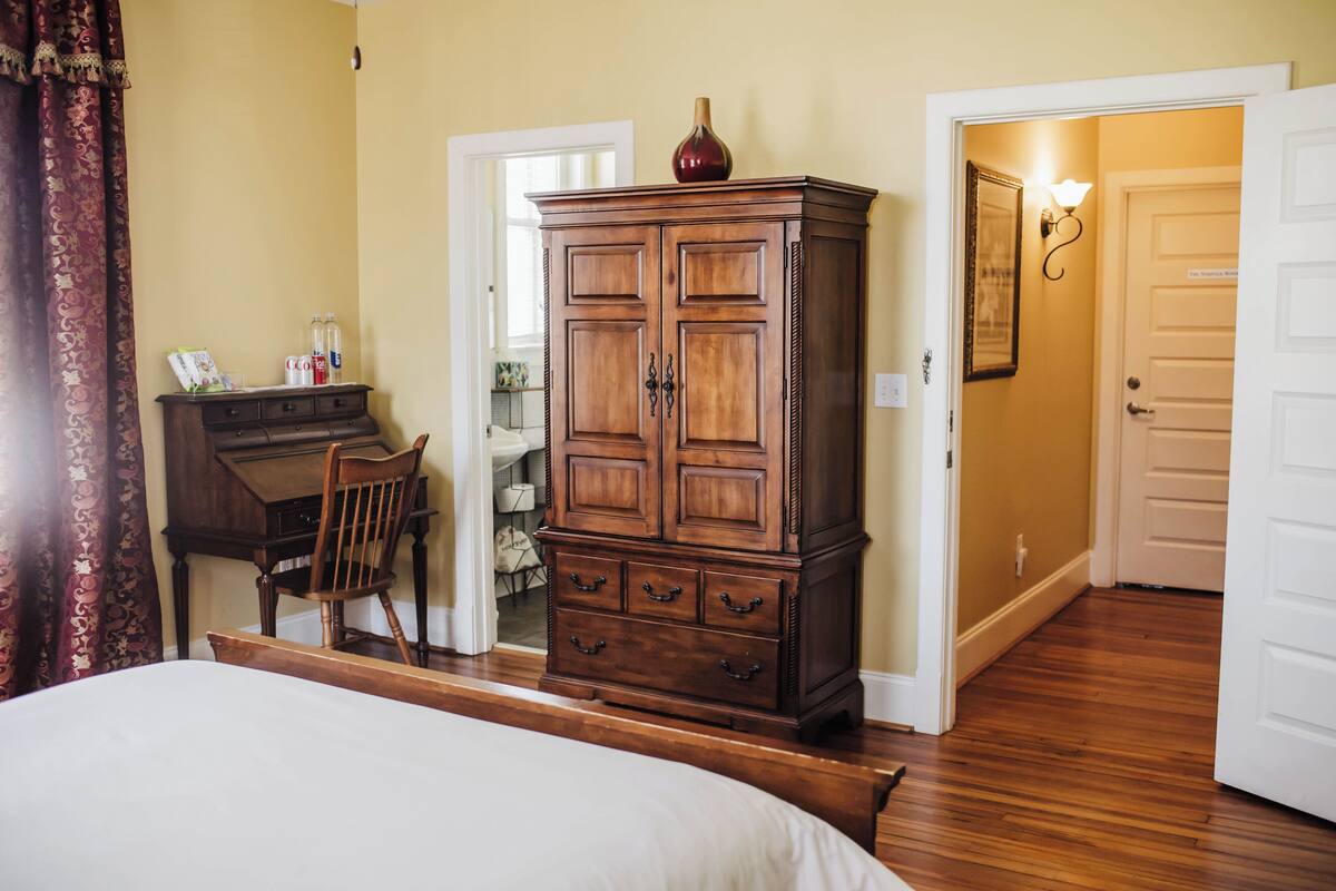 A bedroom with a bed, a wooden dresser, a desk, and a chair.