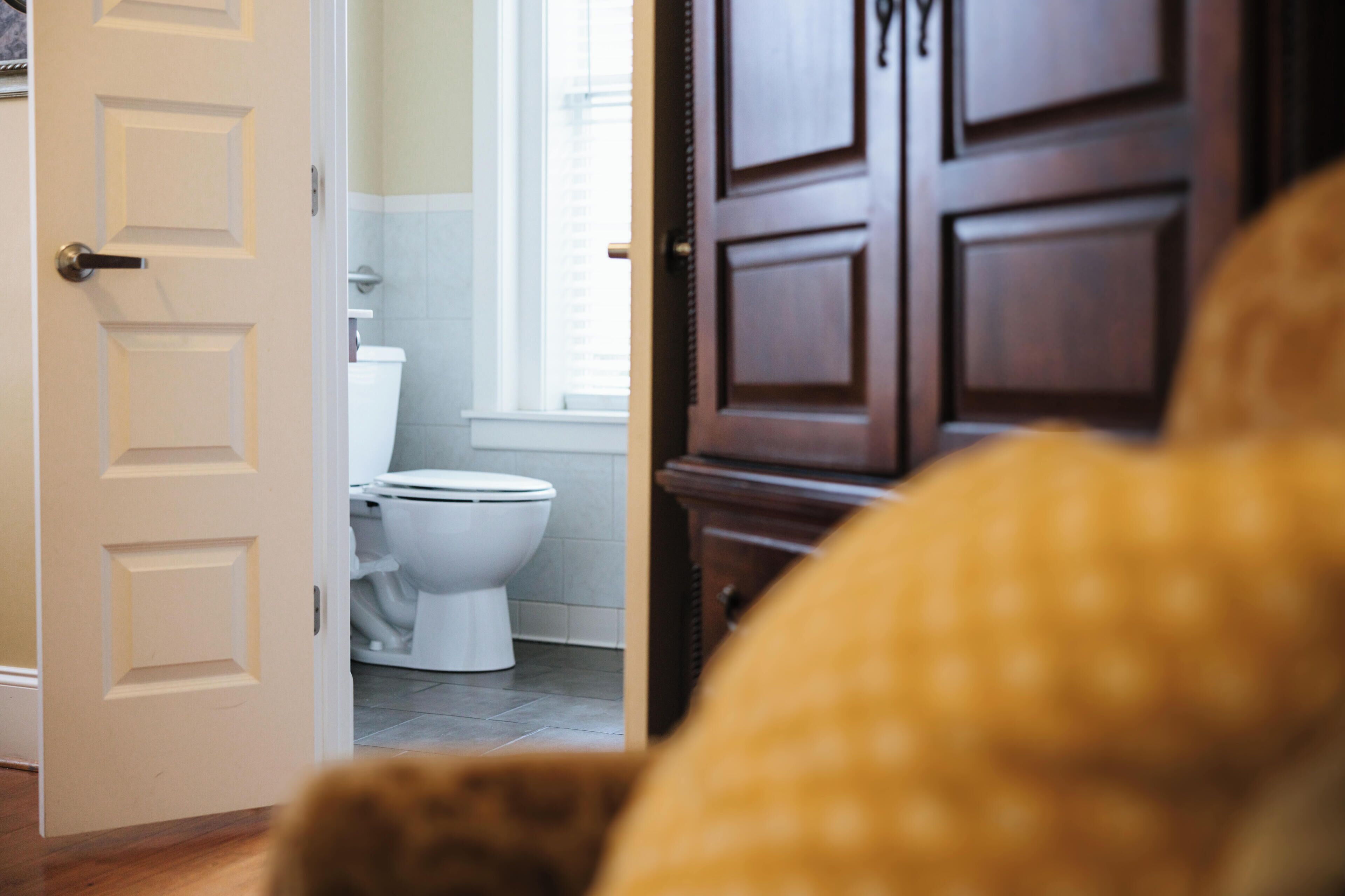 An open door leading to a bathroom with a toilet and a window.