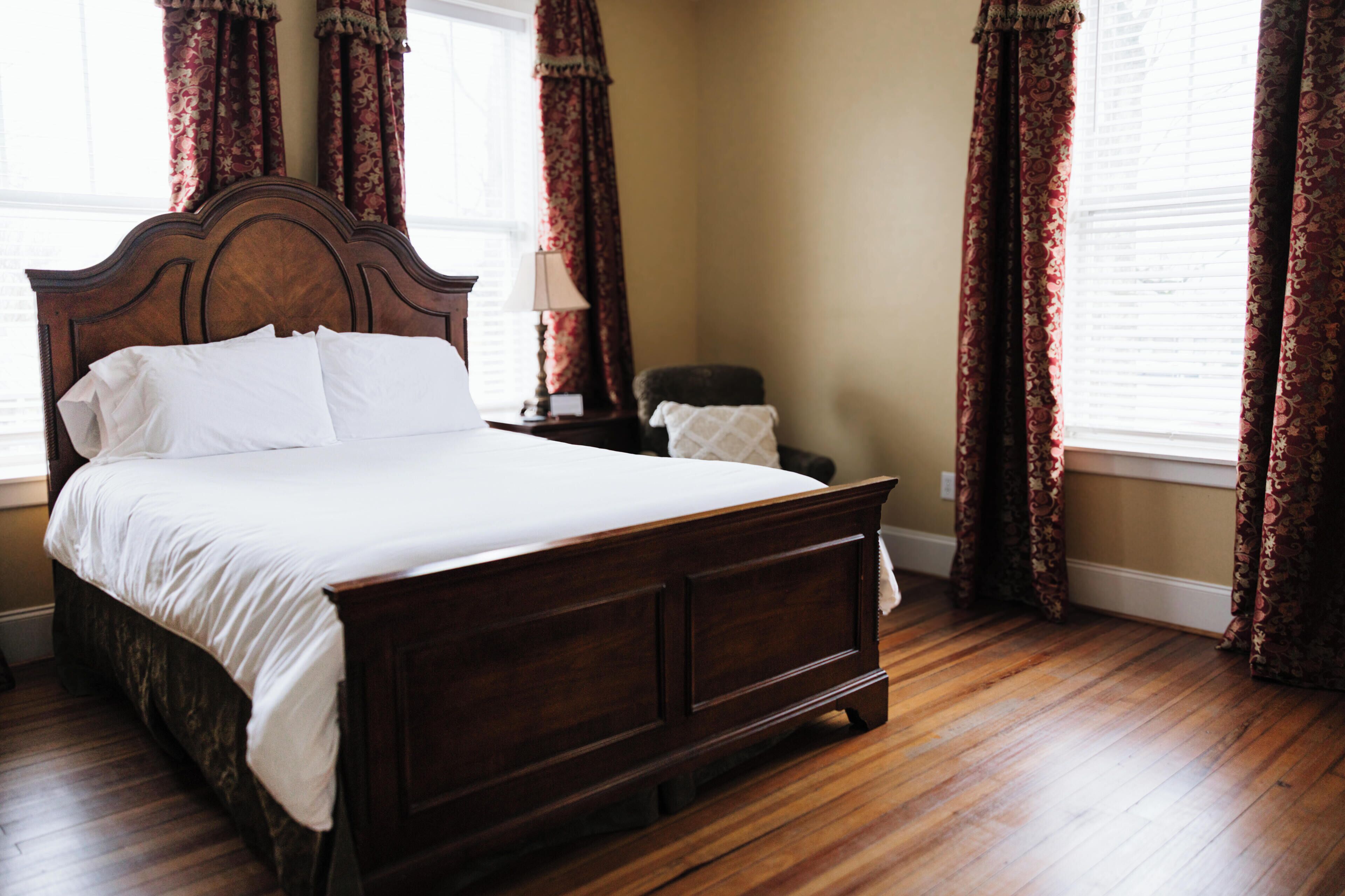 A bedroom with a wooden bed, a nightstand, a chair, and a window with curtains.