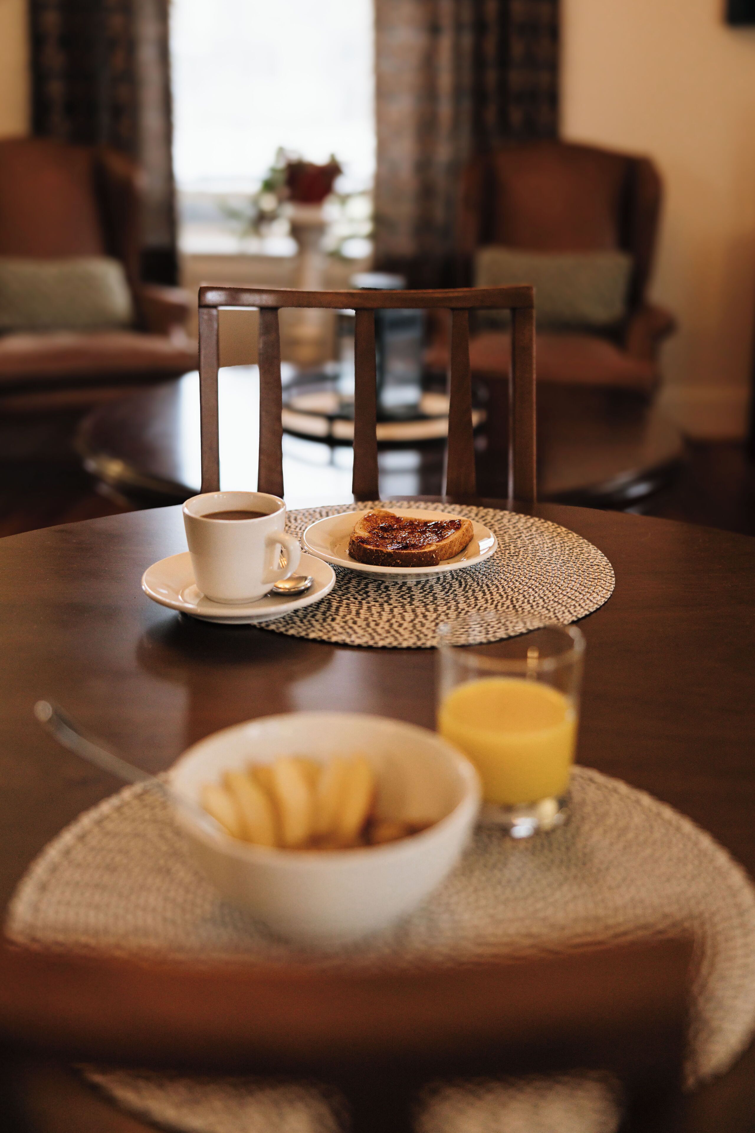 A dining table with a cup of coffee, a plate with toast, and a glass of orange juice.