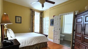 A bedroom with a bed, a bedside lamp, a wooden dresser, and a ceiling fan.