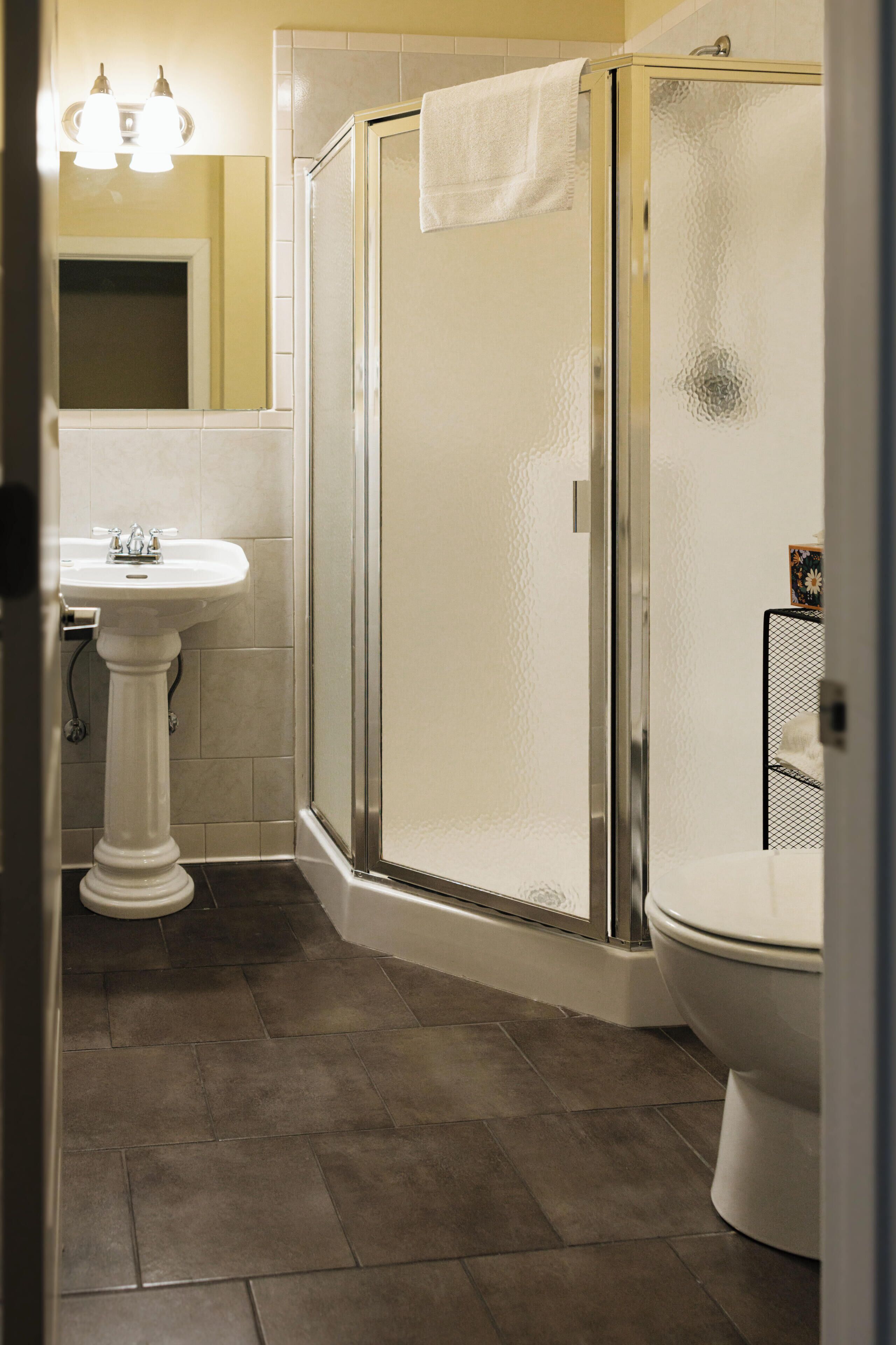 A bathroom with a pedestal sink, a glass-enclosed shower, and a toilet.