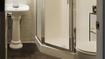 A bathroom with a pedestal sink, a glass-enclosed shower, and a toilet.