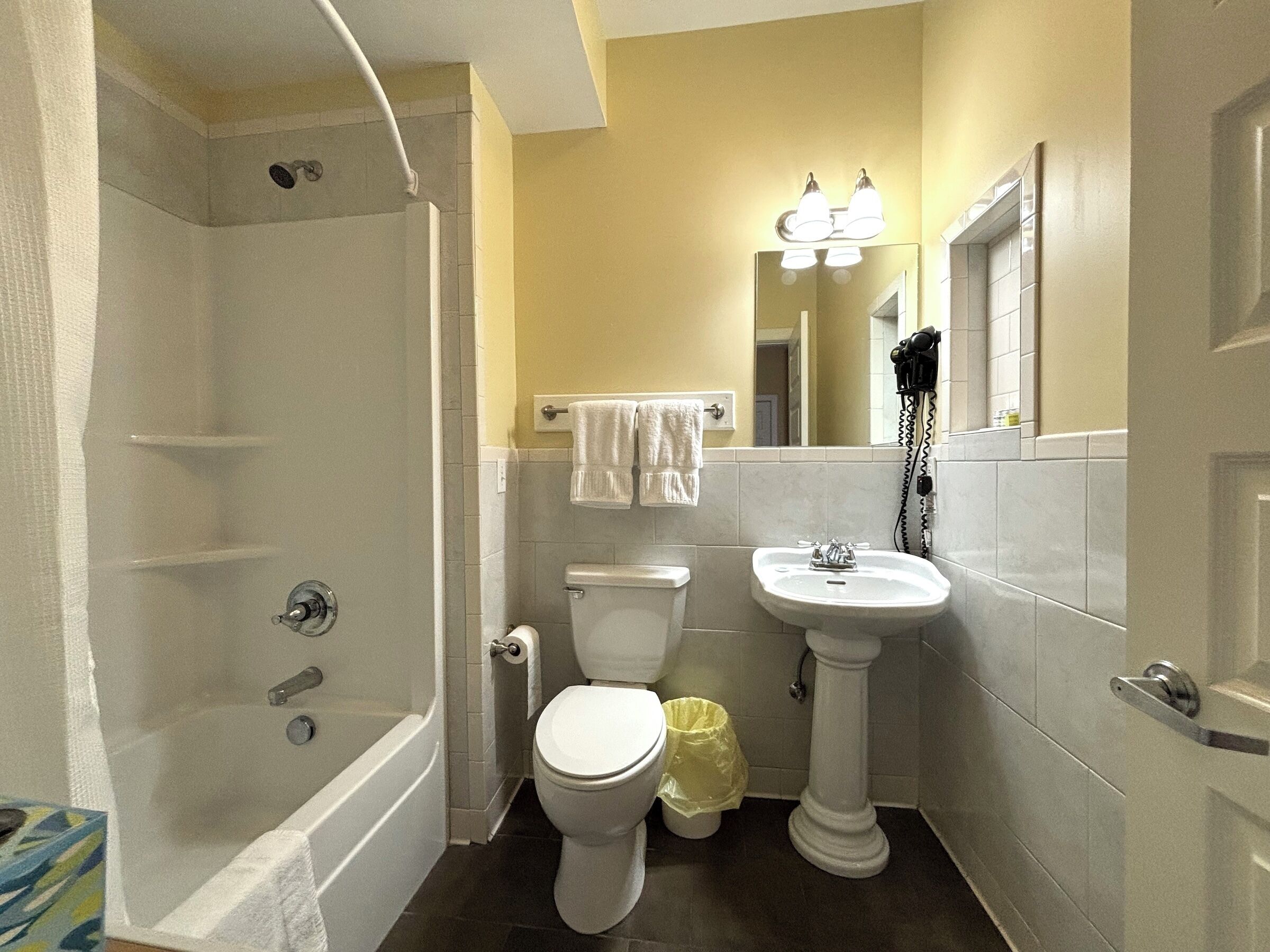 A bathroom with a bathtub, toilet, sink, and a mirror with lights.