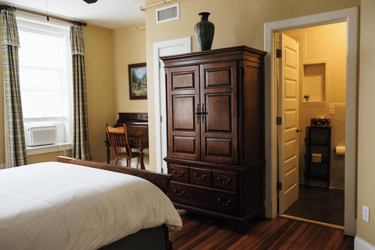 A bedroom with a bed, a wooden cabinet, a desk, and a chair.