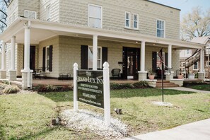 A two-story building with a covered porch, a signboard for The Grand Lux Inn, and a flagpole with an American flag.