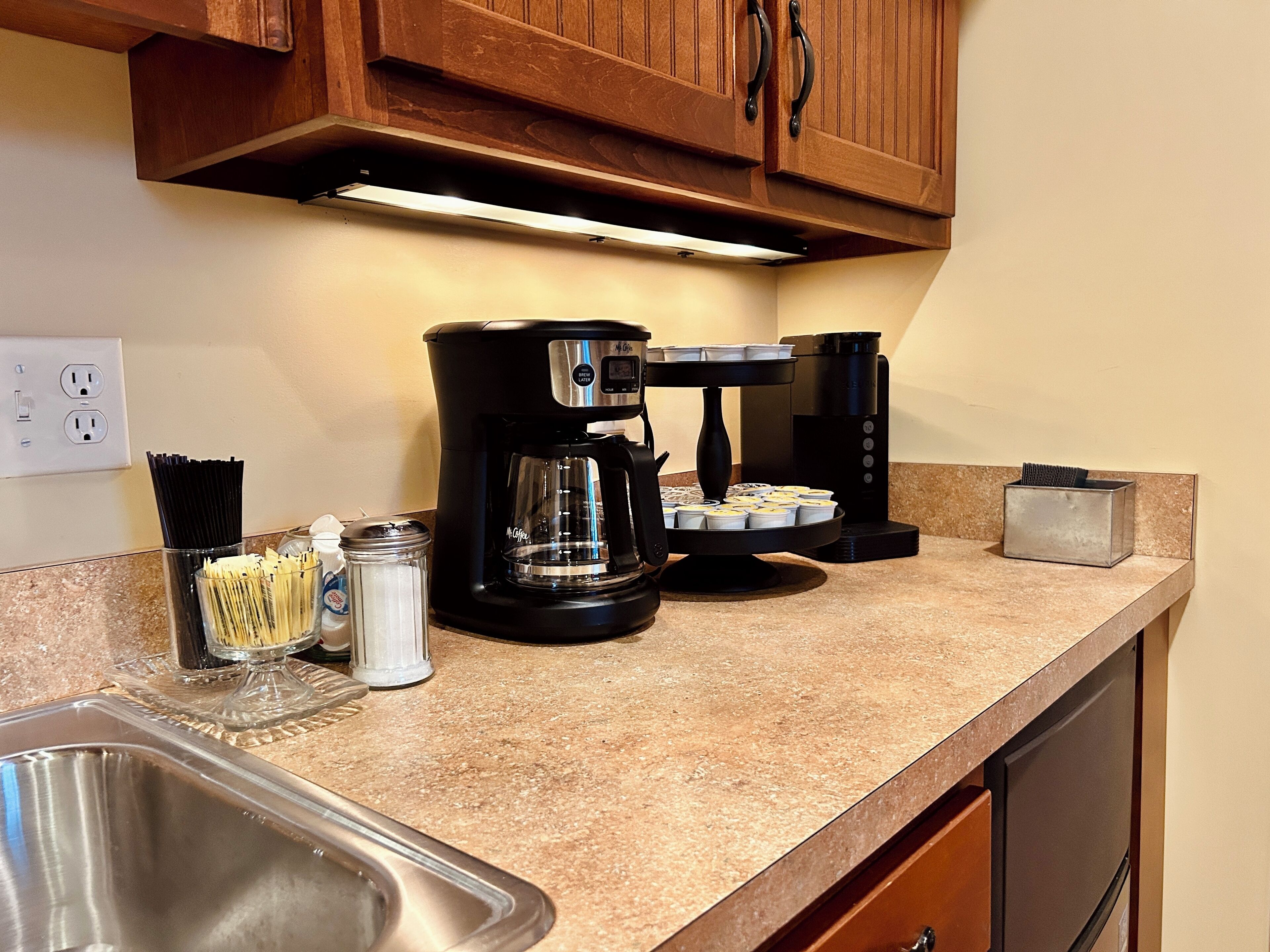 Una cocina con cafetera, un tarro de vidrio y un recipiente metálico sobre la encimera.
