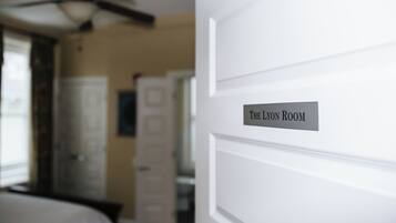 Ein Hotelzimmer mit Deckenventilator, einem Bett, einem Nachttisch und einer Tür mit der Aufschrift 'The Lyon Room'.