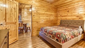 A wooden cabin bedroom with a bed, a ceiling fan, and a small table with chairs. - Quaint Log Cabin-Fire Pit-Waterside Property-Birds Creek Campground (Sevierville)