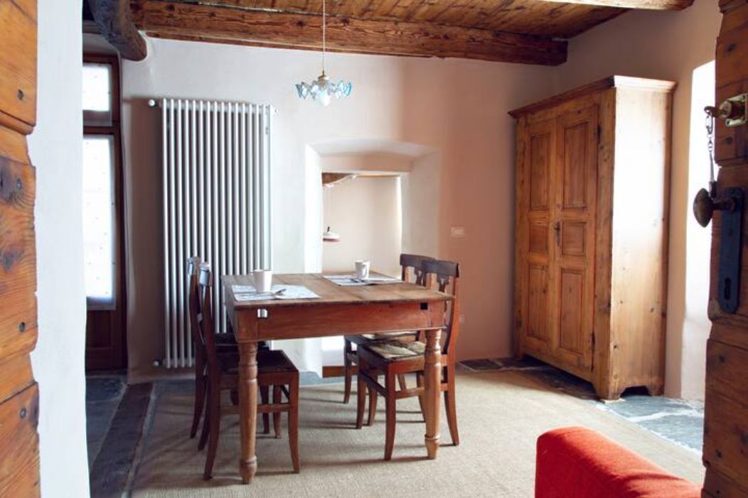 A wooden dining table with chairs, a chandelier, and a wooden cabinet in a room with a sloped ceiling and a radiator.