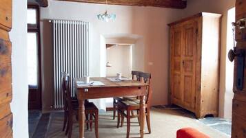 A wooden dining table with chairs, a chandelier, and a wooden cabinet in a room with a sloped ceiling and a radiator.