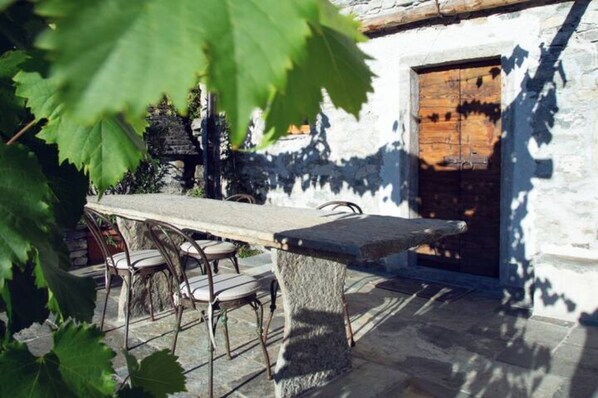 A stone table with chairs in front of a rustic building with a wooden door.