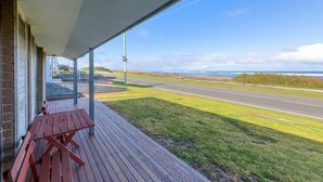 A covered outdoor area with a wooden bench, a view of a road, and the ocean in the distance. - Seaclusion - Beachside Luxury (Port Fairy)