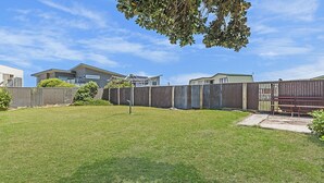 A backyard with a wooden fence, a grassy lawn, and a bench. - Seaclusion - Beachside Luxury (Port Fairy)