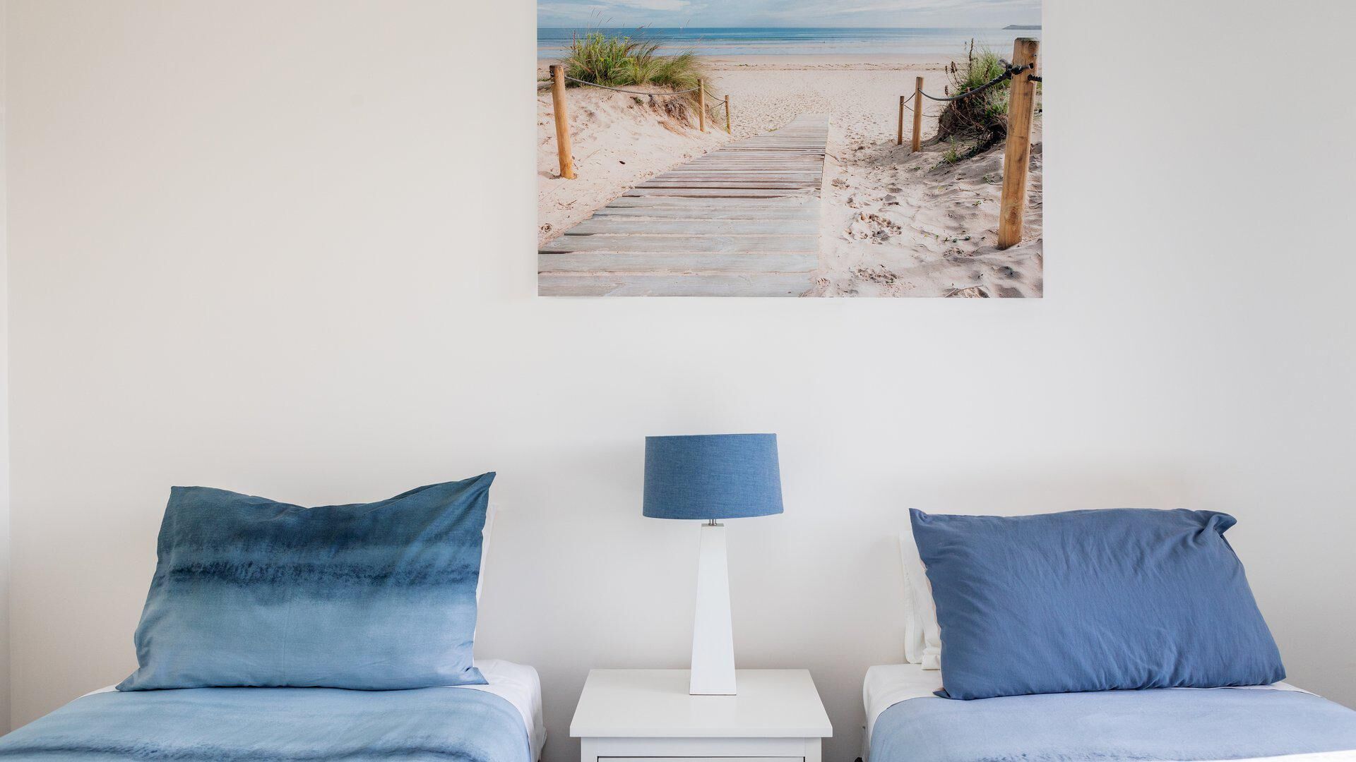 Une chambre avec deux lits, une table de chevet avec une lampe et une décoration murale représentant une scène de plage.