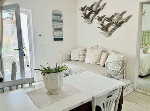 A room with a white bed, a white table with a plant, a wall with decorative bird art, and a sign with family rules.