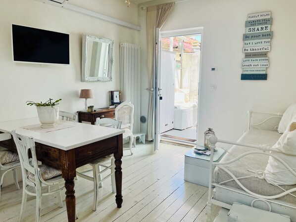 A room with a wooden dining table, white chairs, a white bed, and a white radiator.