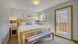 Ein Schlafzimmer mit einem hölzernen Bett, einer Bank, einem Nachttisch, einer Lampe und einer Tür, die auf einen Balkon führt.