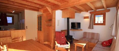 A wooden interior with a dining table, chairs, a sofa, a TV, and a fireplace.