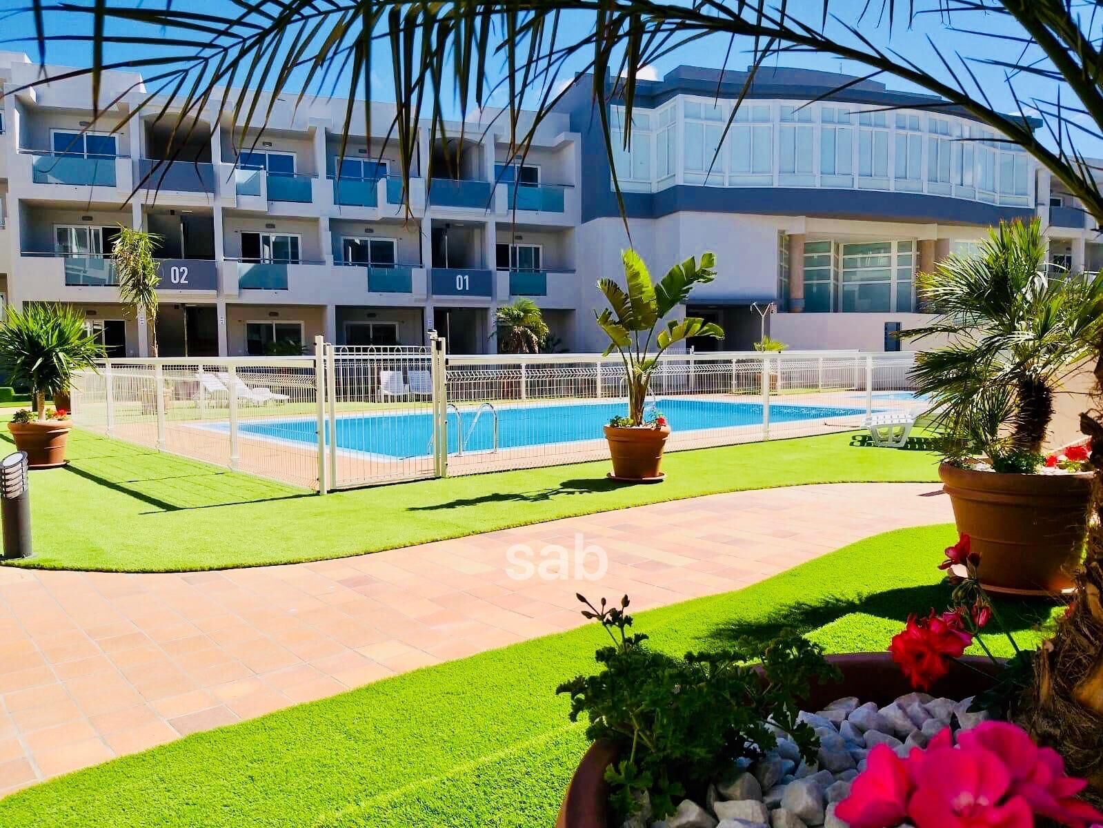 A hotel with a pool area, multiple balconies, and a well-maintained lawn.