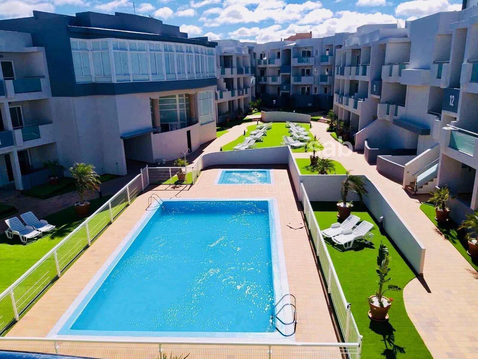 Un hotel moderno con piscina central, varios balcones y un c ésped bien cuidado.