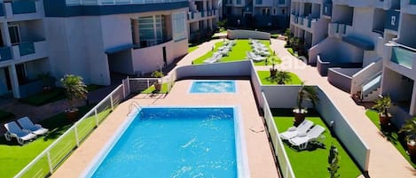 Et moderne hotel med central pool, flere balkoner og en velholdt græsplæde.