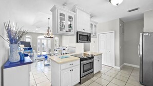 Una cocina moderna con armarios blancos, un refrigerador de acero inoxidable y una isla central con un microondas arriba.