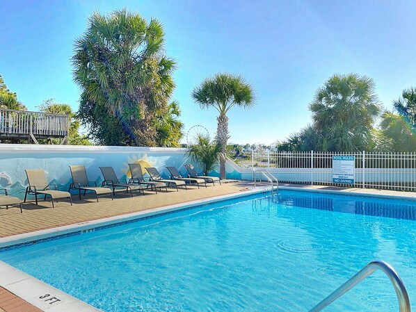 A swimming pool with lounge chairs and a sign indicating pool rules.