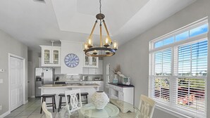 Una cocina moderna con armarios blancos, una isla central y un comedor con mesa y sillas de vidrio.