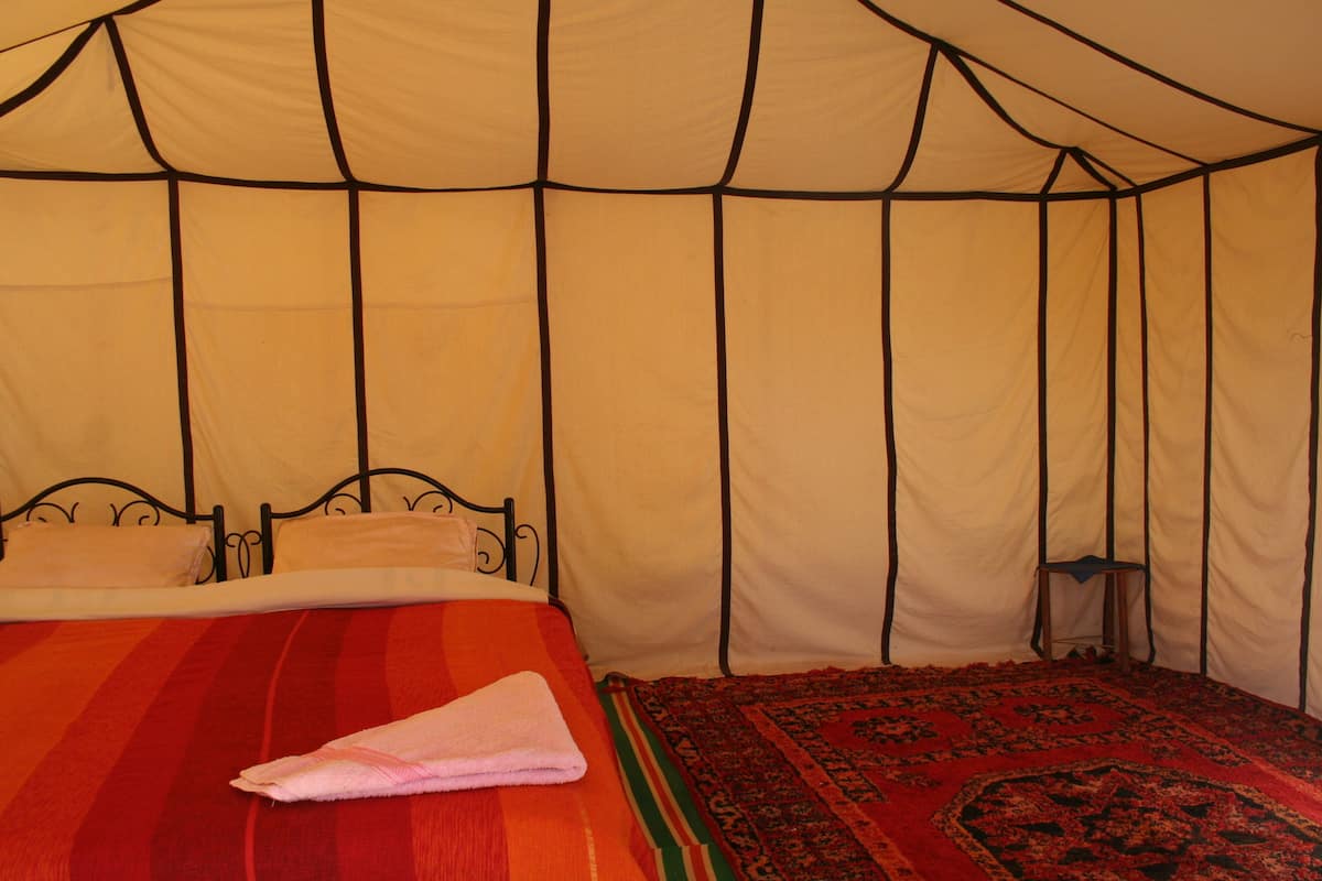 Een tent met een bed, een klein tafeltje en een kamerkleed met dessin.