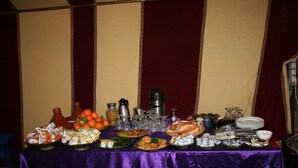 A table with various food items and kitchenware, set against a striped wall. - Zagora Desert Camp (Errouha)