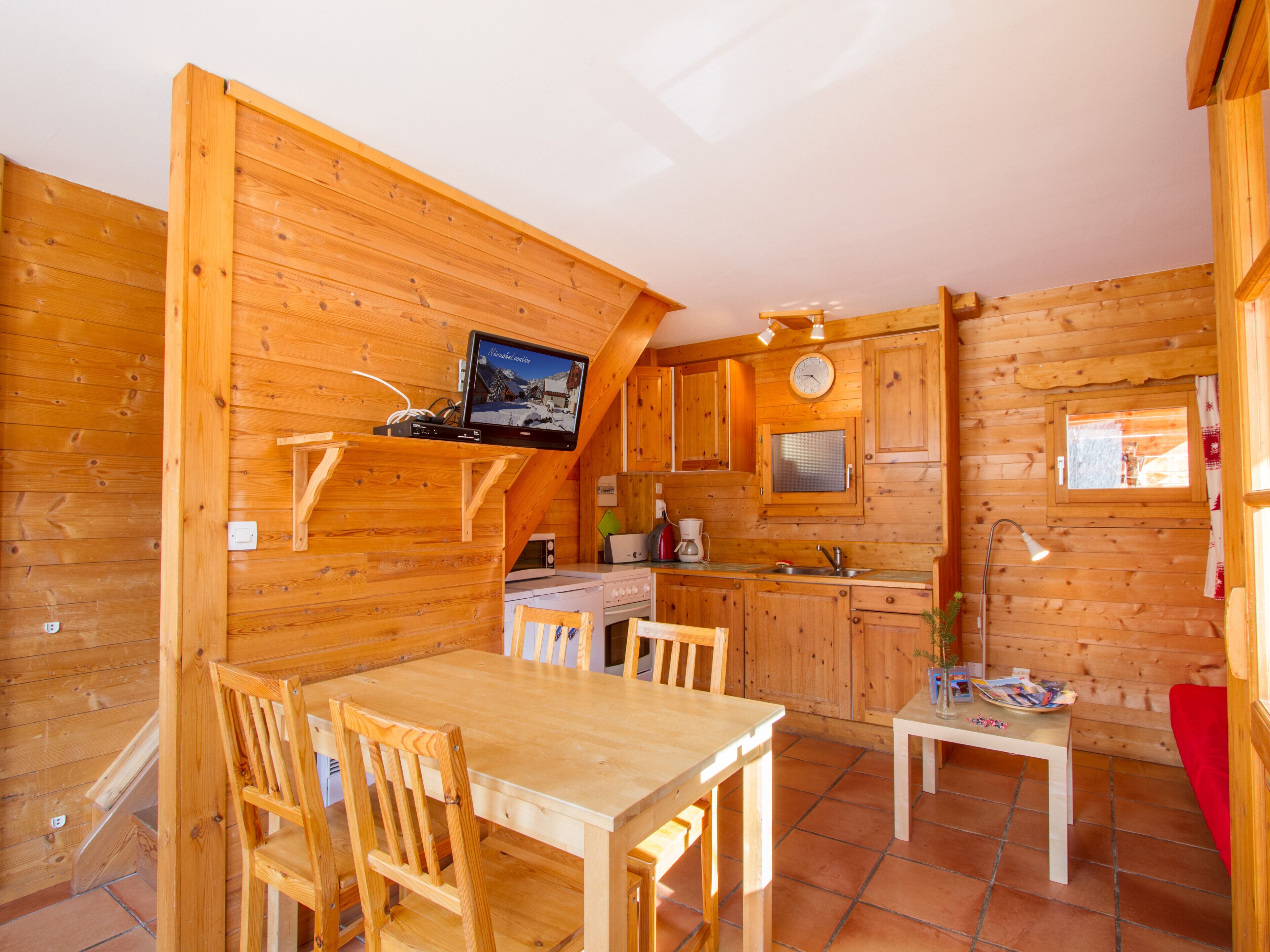 L’intérieur d’un chalet en bois comprend un coin repas, une cuisine et un téléviseur qui diffuse des images d’un paysage enneigé.