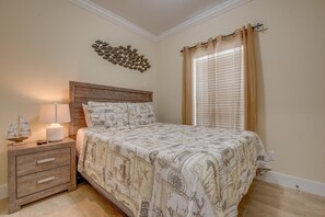 A bedroom with a wooden nightstand, a lamp, a bed with a patterned bedspread, a wall decoration, and a window with curtains.