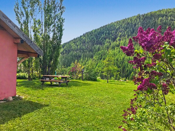 A grassy area with a picnic table, a building, and a forested hillside. - Le troll: family chalet, valley views and skiing nearby (Névache)