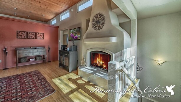 A cozy living room with a fireplace, wooden ceiling, and a large window. - Eagles Rest Dog Friendly | Soar, Slow Down, and Stay Above It All in Ruidoso (Ruidoso)