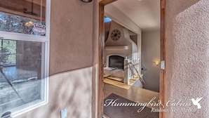 A hallway with a wooden door leading to a living area with a fireplace and a clock on the wall. - Eagles Rest Dog Friendly | Soar, Slow Down, and Stay Above It All in Ruidoso (Ruidoso)