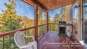 A covered porch with a grill and chairs, overlooking a forested area. - Eagles Rest Dog Friendly | Soar, Slow Down, and Stay Above It All in Ruidoso (Ruidoso)