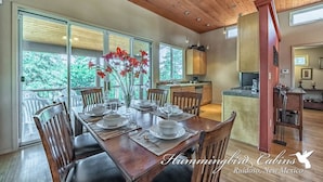 A dining area with a wooden table set for six, surrounded by chairs, with a view of trees through large windows. - Eagles Rest Dog Friendly | Soar, Slow Down, and Stay Above It All in Ruidoso (Ruidoso)