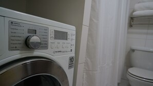 Eine Waschmaschine mit Frontlader, digitalem Display und Bedienfeld in einem Badezimmer mit Toilette und Duschvorhang.