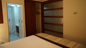 Ein Schlafzimmer mit Bett, einem Holzschrank, einem Badezimmer mit Toilette und Waschbecken sowie einer Dusche.