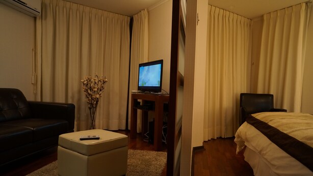 Ein Hotelzimmer mit einem Bett, einem Fernseher auf einem Schrank, einer Couch und einem kleinen Tisch mit einer Fernbedienung.