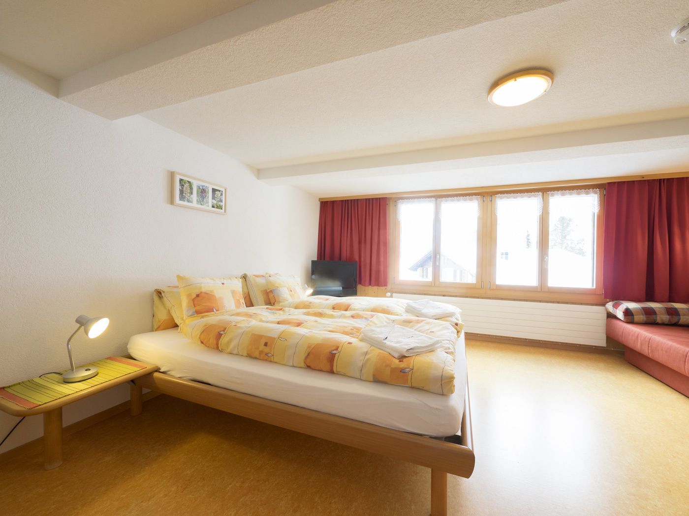 A bedroom with a bed, a desk with a lamp, a television, and a window with curtains.
